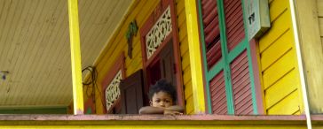 Kleines Kind schaut von gelb gestrichenem Balkon herunter