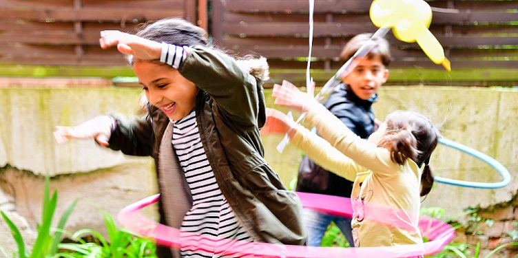 Drei Kinder spielen mit Hula-Hoop-Reifen und gelbem Luftballon